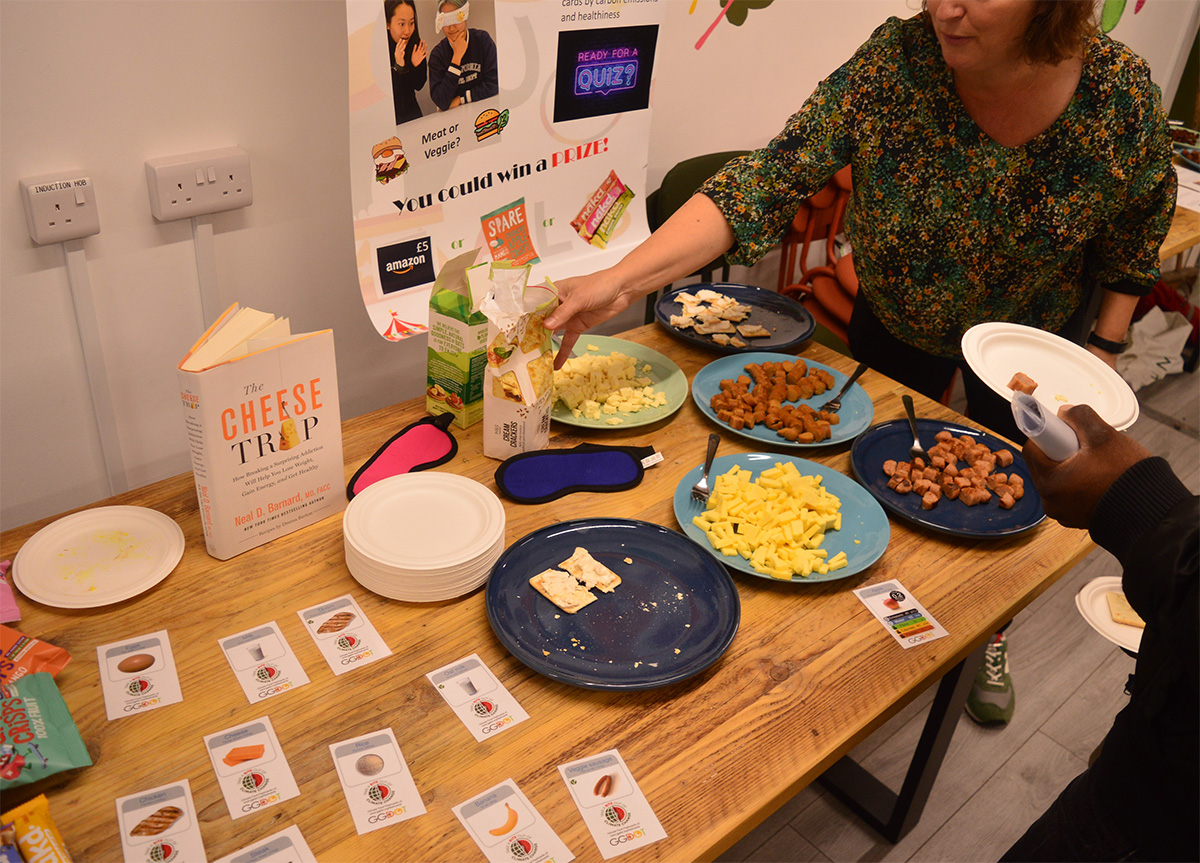 Several food items sit on plates with coloured labels and a woman holding out a packet of crackers.