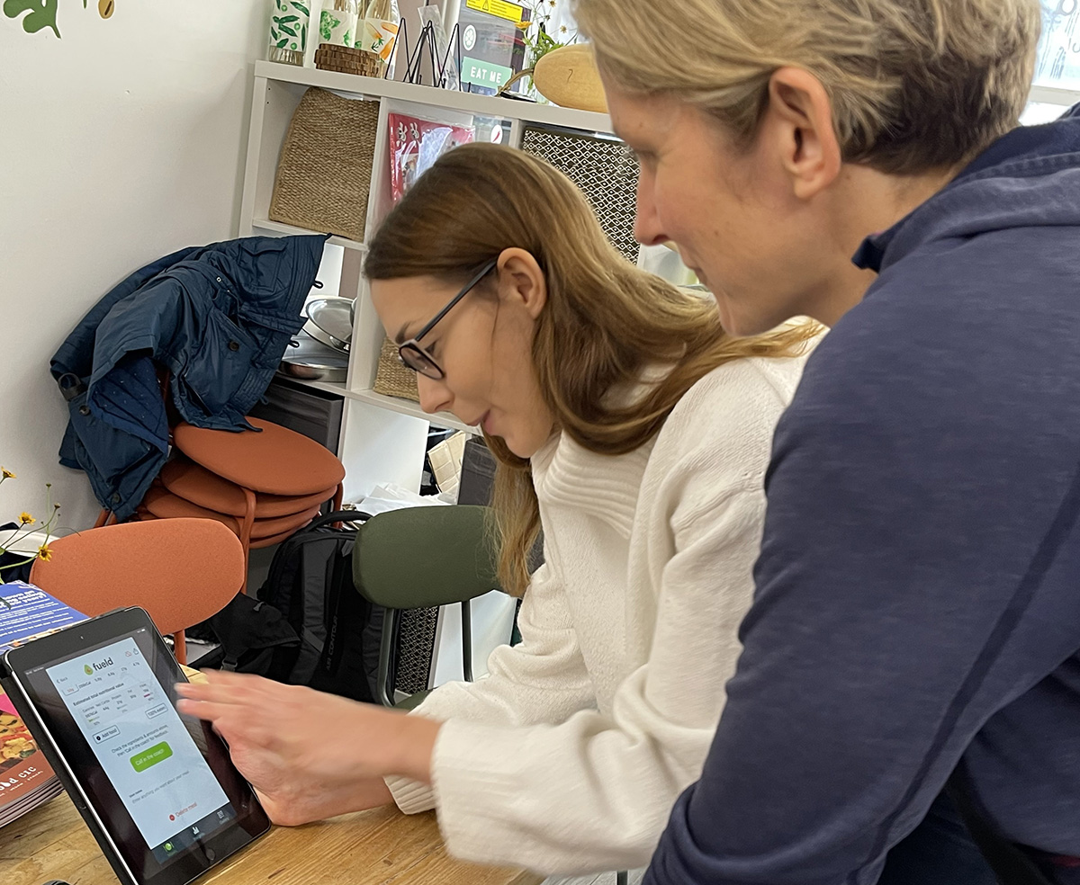 Two people (women) in conversation lean over a table using an iPad.