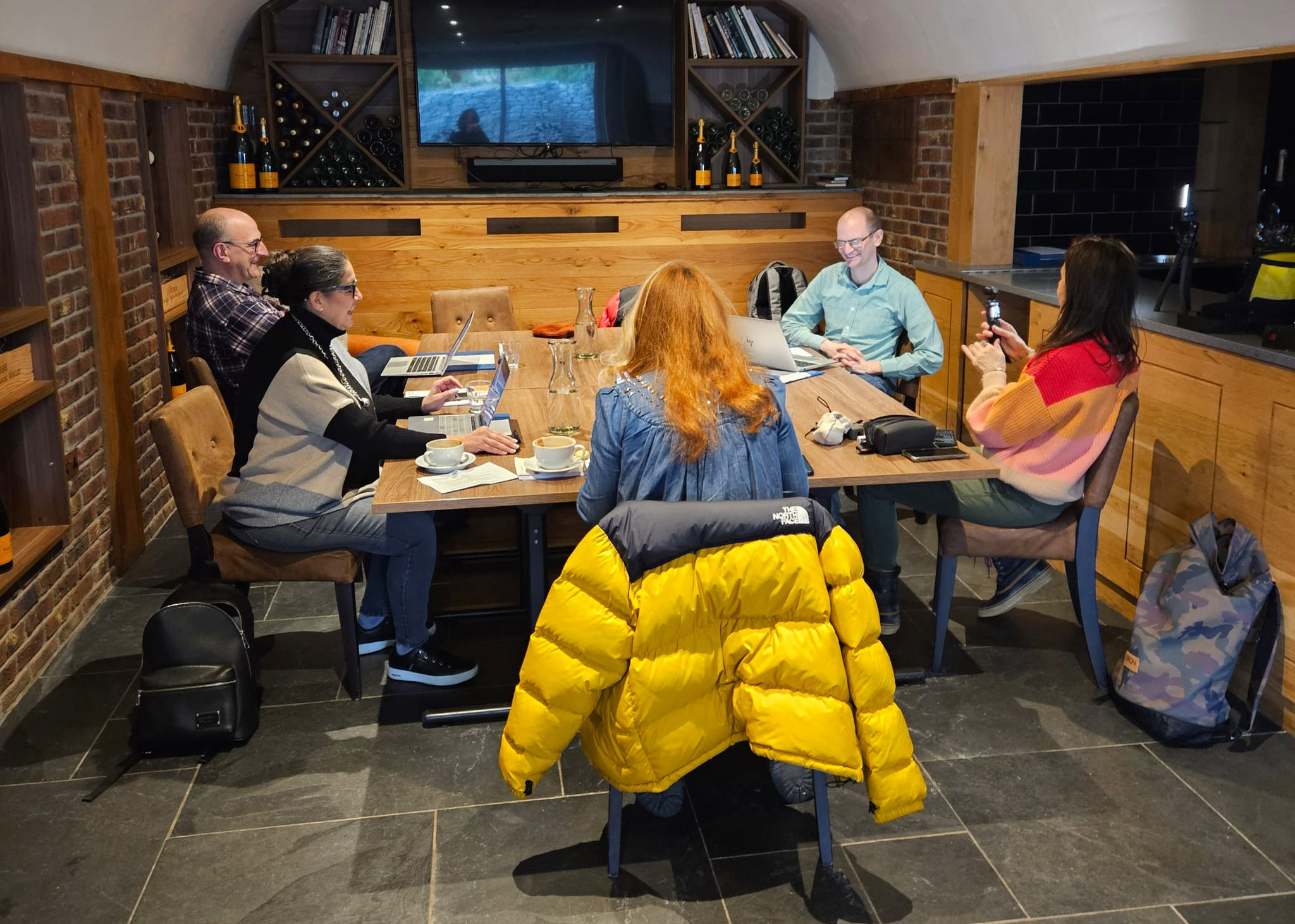 People sit smiling around a large desk in a room with wood and brick walls